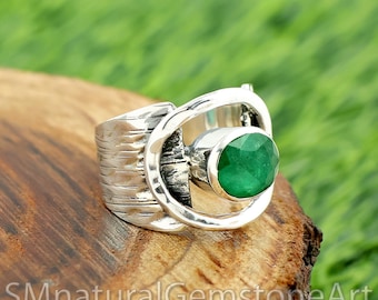 Puede incluir: Un anillo de plata con una gran esmeralda ovalada. El anillo tiene una banda texturizada y un diseño calado único alrededor de la esmeralda. La piedra preciosa es de color verde vibrante, engastada en una montura de plata pulida.