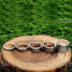 Op de afbeelding: Vijf zilveren ringen in verschillende maten worden getoond op een houten oppervlak. De ringen zijn allemaal glad en hebben een licht getextureerde afwerking. De ringen zijn aan de binnenkant gemarkeerd met het nummer "925".