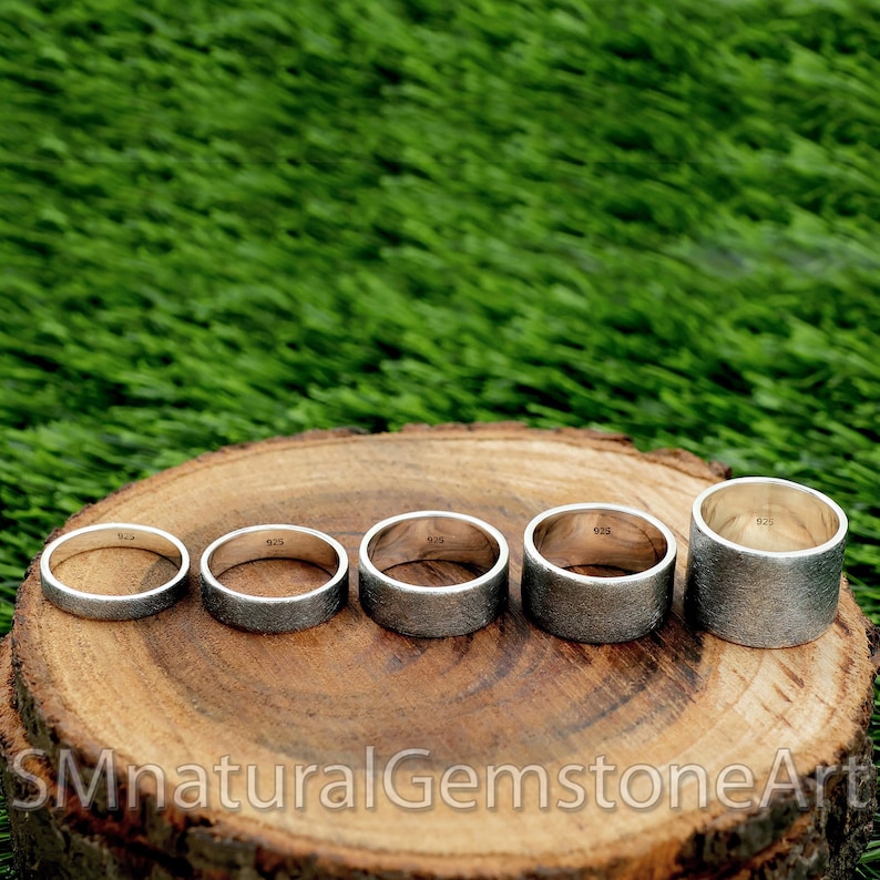 Op de afbeelding: Vijf zilveren ringen in verschillende maten worden getoond op een houten oppervlak. De ringen zijn allemaal glad en hebben een licht getextureerde afwerking. De ringen zijn aan de binnenkant gemarkeerd met het nummer "925".