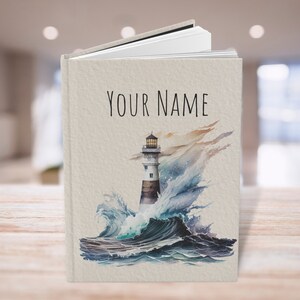 Puede incluir: Un diario personalizado con una ilustraci&oacute;n de acuarela de un faro en un mar tormentoso. El texto "YOUR NAME" est&aacute; impreso en la portada.