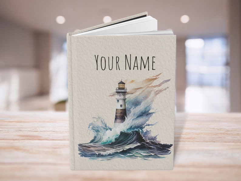 Puede incluir: Un diario personalizado con una ilustraci&oacute;n de acuarela de un faro en un mar tormentoso. El texto "YOUR NAME" est&aacute; impreso en la portada.