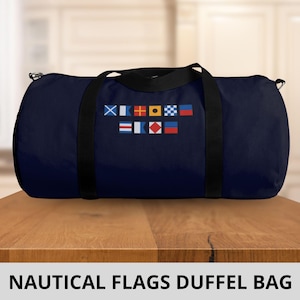Könnte beinhalten: Eine marineblaue Reisetasche mit schwarzen Riemen und einem Design aus nautischen Flaggen in Rot, Gelb, Blau und Weiß. Der Text "NAUTICAL FLAGS DUFFEL BAG" ist unter der Tasche aufgedruckt.
