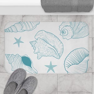 May include: A white bath mat featuring a blue seashell and starfish design. The mat is made from a soft, absorbent material and is ideal for adding a touch of coastal style to your bathroom.