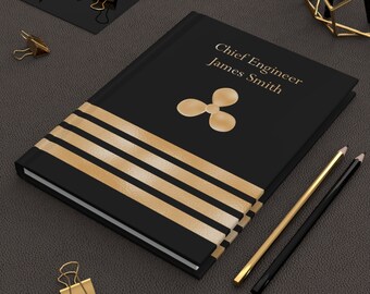 May include: Black leather journal with gold stripes and a gold propeller design. The text "Chief Engineer James Smith" is printed on the cover.