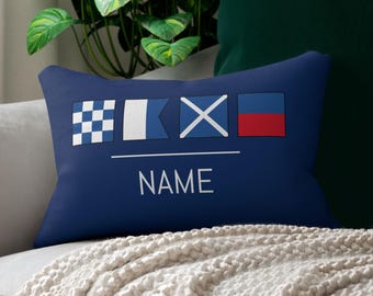 Könnte beinhalten: Marineblaues rechteckiges Kissen mit nautischen Signalflaggen und dem Wort "NAME" in Weiß. Das Kissen zeigt vier Signalflaggen mit verschiedenen Mustern und Farben, ideal für eine nautische Dekoration.