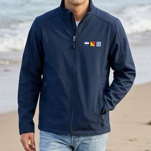 May include: A navy blue softshell jacket featuring a mock neck collar, a full-length front zipper, and two zippered side pockets. On the left chest, there are three small square nautical signal flags in blue, white, yellow, and red colors.
