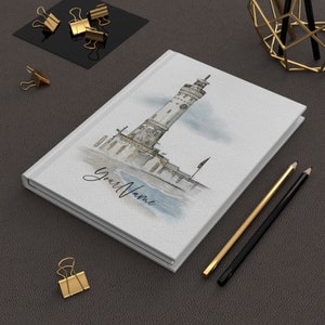 May include: White notebook with a watercolour illustration of a lighthouse on the cover. The notebook has the text "Your Name" printed on the front.