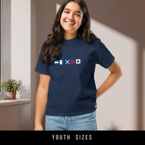 May include: A navy blue youth t-shirt with a white, blue, and red nautical flag design. The flags are arranged in a row across the chest of the shirt.