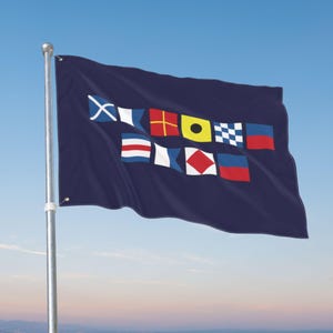 May include: A dark navy blue rectangular flag attached to a silver metal pole. The flag features two horizontal rows of colourful nautical signal flags printed in the centre, displaying various geometric patterns including crosses, squares, and diamonds.