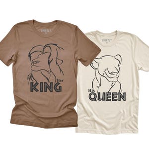May include: Two short-sleeved t-shirts. One is brown with a lion graphic and the text "Her King". The other is off-white with a lioness graphic and the text "His Queen".