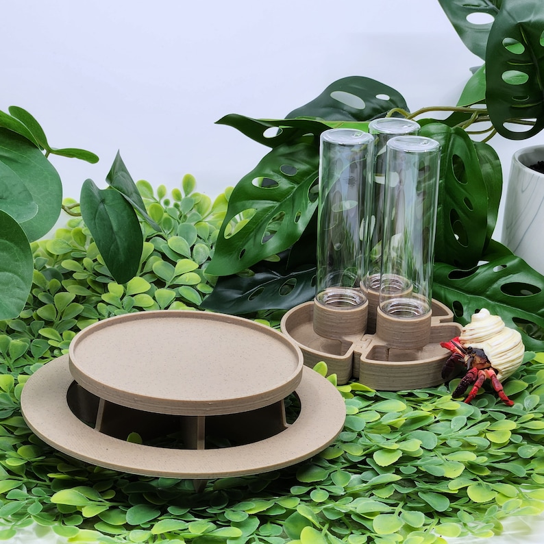 May include: A tan, circular, multi-tiered platform with a flat top and a wide base, accompanied by a separate tan, circular base featuring three vertical, clear, cylindrical glass tubes arranged in a cluster for display or storage purposes.