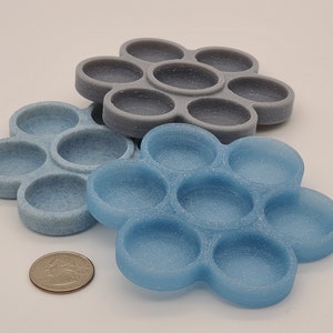 May include: Two silicone fidget toys in the shape of a flower with seven circles. The top toy is grey and the bottom toy is blue.