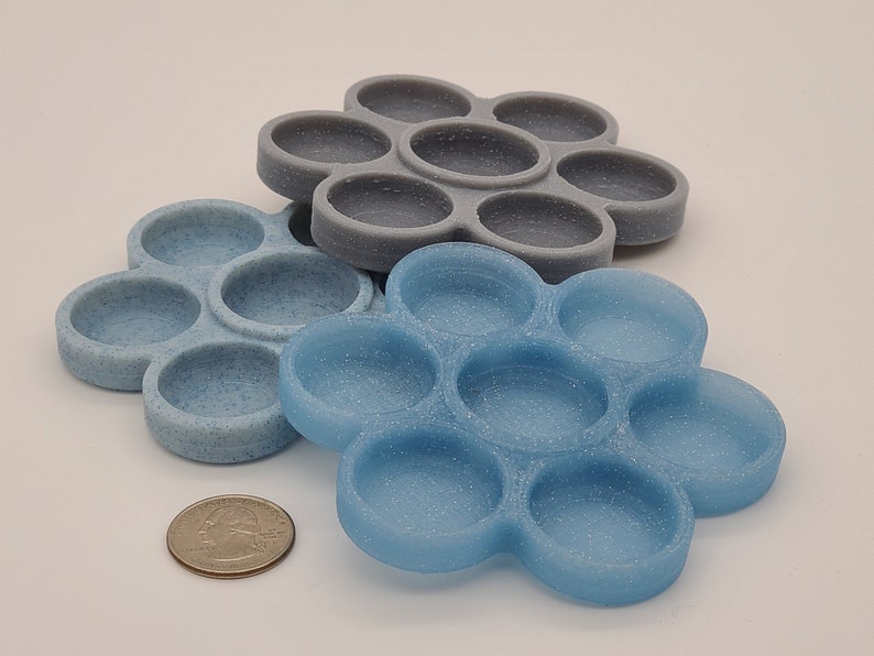 May include: Two silicone fidget toys in the shape of a flower with seven circles. The top toy is grey and the bottom toy is blue.