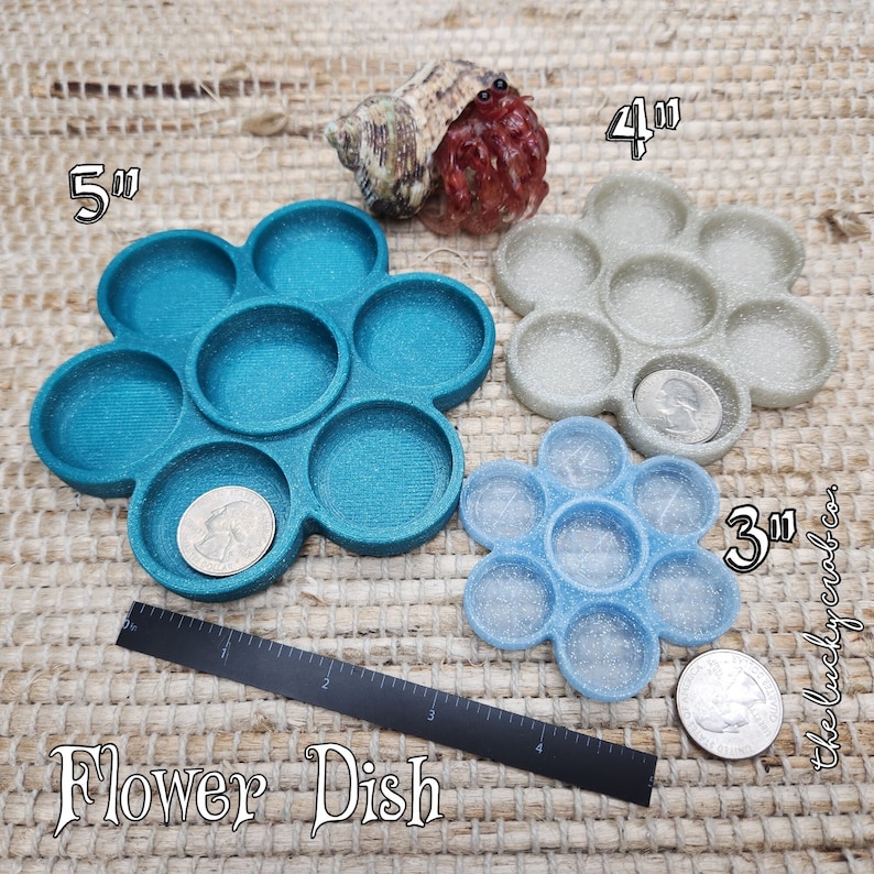May include: Three flower-shaped paint palettes in different sizes: 5 inches, 4 inches, and 3 inches. The palettes are teal, grey, and light blue with a sparkly finish. The text "Flower Dish" is printed below the palettes.