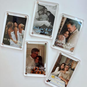 Puede incluir: Cinco marcos de fotos rectangulares de acrílico transparente con herrajes plateados, cada uno con una fotografía diferente y superposiciones de texto en blanco que incluyen frases como MY SOMETHING BLUE, Can't say I do without you, DADDY'S GIRL forever y No love like a mother's love.