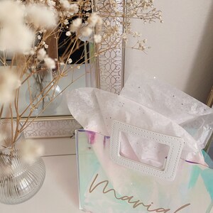 May include: A clear iridescent tote bag with a white handle and the name "Mariah" written in gold script.