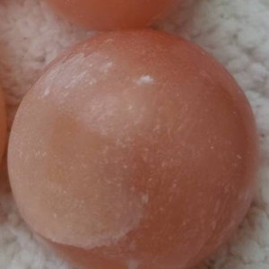 May include: Two smooth, round, light pink Himalayan salt stones. The stones have a slightly rough texture and are perfect for massage or relaxation.
