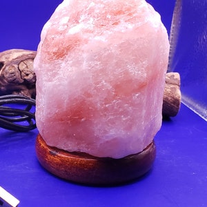 K&ouml;nnte beinhalten: Eine rosa Himalaya-Salzlampe mit einem Holzsockel. Die Lampe ist mit einem USB-Kabel angeschlossen.