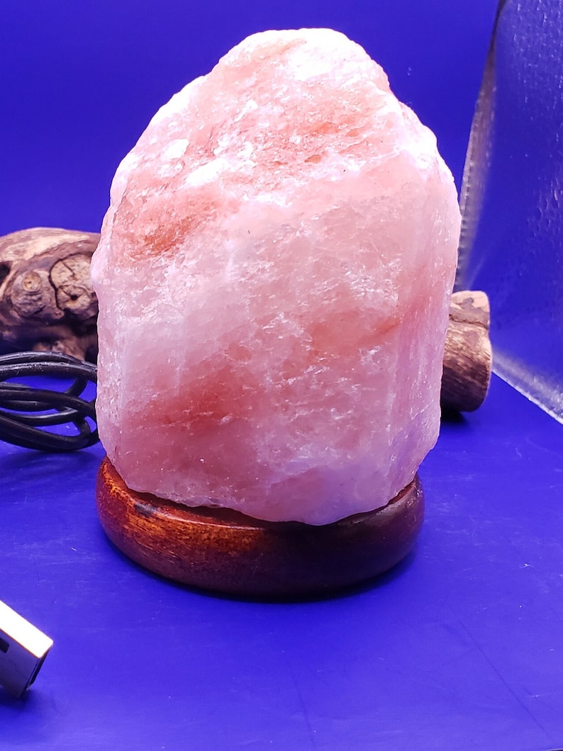 K&ouml;nnte beinhalten: Eine rosa Himalaya-Salzlampe mit einem Holzsockel. Die Lampe ist mit einem USB-Kabel angeschlossen.
