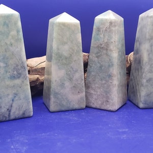 May include: Six blue and white agate crystal points, also known as blue lace agate, arranged in a row on a blue surface. The points are polished and have a smooth, glassy finish.