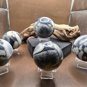 May include: Five polished black and white marble spheres on clear acrylic stands. The spheres are arranged on a wooden surface with a dark brown background.