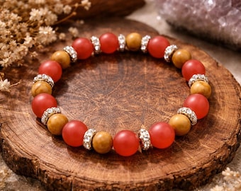 May include: A beaded bracelet featuring alternating red and tan-colored beads, accented with silver-toned spacers. The bracelet is displayed on a rustic wooden surface, with dried flowers and a crystal in the background. A beautiful piece of jewelry.