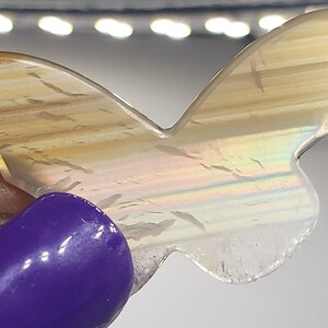 May include: A butterfly-shaped agate stone with a brown, white, and iridescent finish. The stone has a natural, organic shape and a smooth, polished surface.