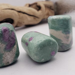 May include: Three tumbled stones with a green and white base and pink accents. The stones are smooth and polished.