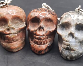 May include: Three carved skull keychains made of red and grey stone. The keychains are attached to silver key rings.