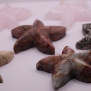 May include: Five different colored stone starfish, each with a unique pattern. The starfish are made of pink, brown, gray, and white stone.