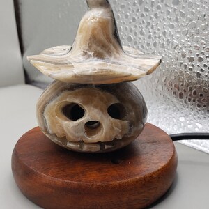 May include: A carved alabaster pumpkin with a witch's hat, sitting on a wooden base.
