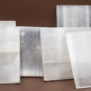 May include: A collection of seven clear, rectangular selenite crystals of varying sizes. The crystals are smooth and have a slightly cloudy appearance.