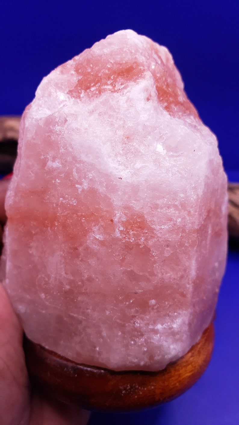 K&ouml;nnte beinhalten: Eine gro&szlig;e, rosafarbene Himalaya-Salzlampe mit einem Holzsockel. Die Salzlampe hat eine unregelm&auml;&szlig;ige Form und eine raue, strukturierte Oberfl&auml;che.