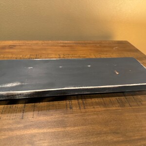 May include: A black wooden shelf with a distressed white paint finish. The shelf is rectangular and has a smooth surface.