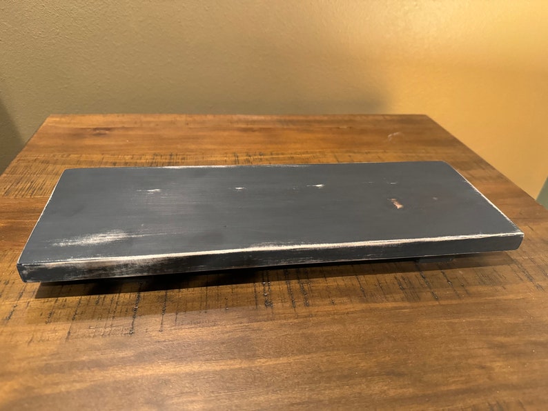 May include: A black wooden shelf with a distressed white paint finish. The shelf is rectangular and has a smooth surface.