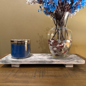 May include: A whitewashed wooden tray with a blue candle and a glass vase filled with blue flowers and red and white glass stones.