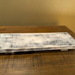 May include: A rustic wooden tray with a whitewashed finish and distressed edges. The tray has a natural wood grain and is perfect for displaying decorative items or serving snacks.