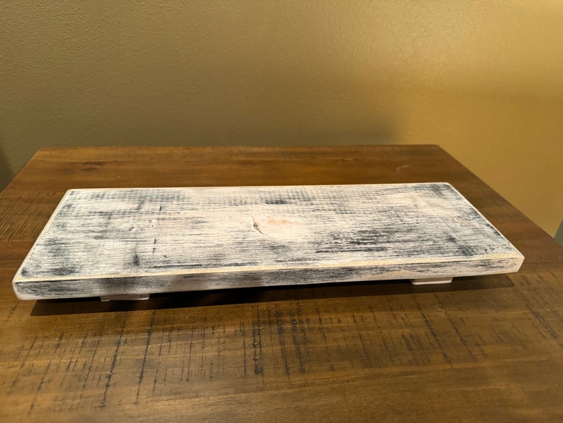 May include: A rustic wooden tray with a whitewashed finish and distressed edges. The tray has a natural wood grain and is perfect for displaying decorative items or serving snacks.
