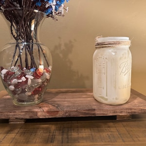 May include: A rustic wooden tray with a clear glass vase filled with red, white, and blue glass stones and a white mason jar with a twine lid. The mason jar has measurements in ounces and cups.