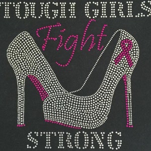 May include: A black t-shirt with a rhinestone design of a high heel shoe. The shoe is outlined in pink rhinestones and the words "Tough Girls Fight Strong" are written in pink rhinestones.