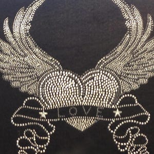 May include: Black fabric with a silver rhinestone design. The design features a heart with wings and the word "LOVE" on a banner, flanked by stars. The wings and heart are detailed with small, sparkling rhinestones.
