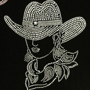 May include: A black graphic design of a woman in a cowboy hat, outlined with sparkling white rhinestones. The hat features a star on its band. The woman's face and hair are also detailed with rhinestones. Suitable for clothing or accessories.