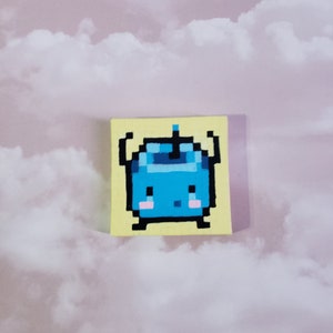 Może przedstawiać: Malowidło pikselowe przedstawiające niebieskie stworzenie na żółtym tle. Stworzenie ma okrągłe ciało, dwie małe ręce, dwie małe nogi i jedną antenę na głowie. Ma uroczy, kreskówkowy wyraz twarzy z dwoma małymi różowymi policzkami.