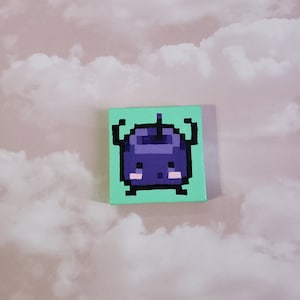 Puede incluir: Una pequeña pintura cuadrada que representa una criatura púrpura pixelada con extremidades negras sobre un fondo verde claro. La obra de arte está situada sobre un fondo de cielo nublado.