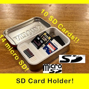 May include: A silver metal container with a white interior holds 10 SD cards and 14 micro SD cards. The container is labeled "10 SD Cards!!" and "14 micro SD!" The container is labeled "VLOID" on the top. The container is sitting on a wooden surface. The text "SD Card Holder!" is written below the container.