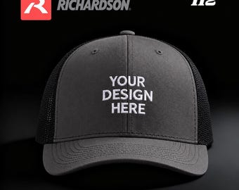 May include: A charcoal gray baseball cap with a black mesh back and a curved brim. The front panel features white embroidered text that reads YOUR DESIGN HERE. The Richardson logo and the number 112 are visible in the upper corners.