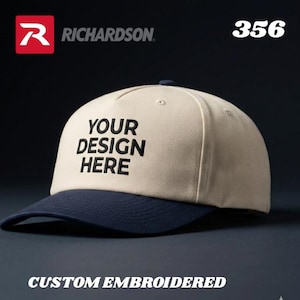 May include: A beige and navy blue baseball cap with the text "YOUR DESIGN HERE" embroidered in black. The cap has a curved brim and a structured crown. The words "CUSTOM EMBROIDERED" are at the bottom.