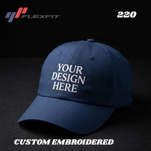 May include: A navy blue Flexfit baseball cap with white embroidered text that reads "YOUR DESIGN HERE." The cap also features the text "CUSTOM EMBROIDERED" and the number "220."