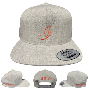 Puede incluir: Gorra snapback gris claro con un dise&ntilde;o bordado en naranja de una letra "J" estilizada con humo. La gorra tiene una visera plana y las palabras "los angeles" y "oakland" en naranja. La parte trasera de la gorra tiene la palabra "umo" en naranja.