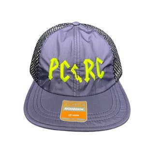 May include: A lavender baseball cap with a black mesh back and a flat brim. The front features the neon yellow embroidered text PC RC with a small vertical shape between the letters. A rectangular Richardson brand sticker is on the brim.